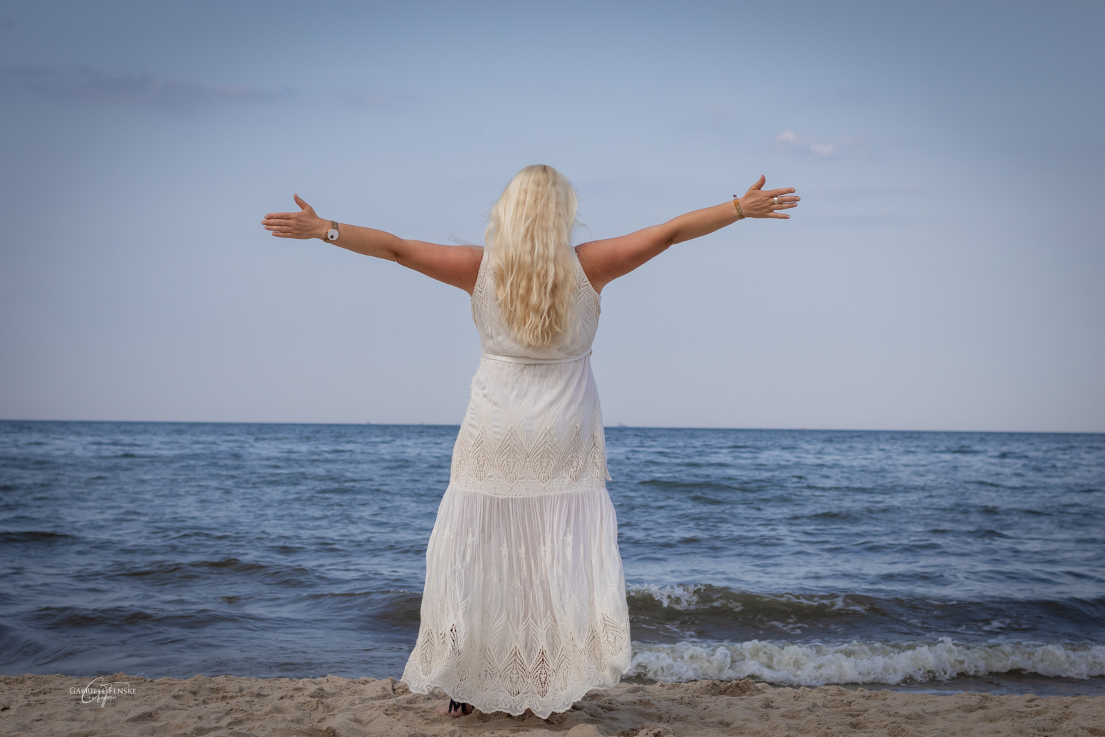 Rückenansicht von Annett Punte am Meer mit ausgebreiteten Armen